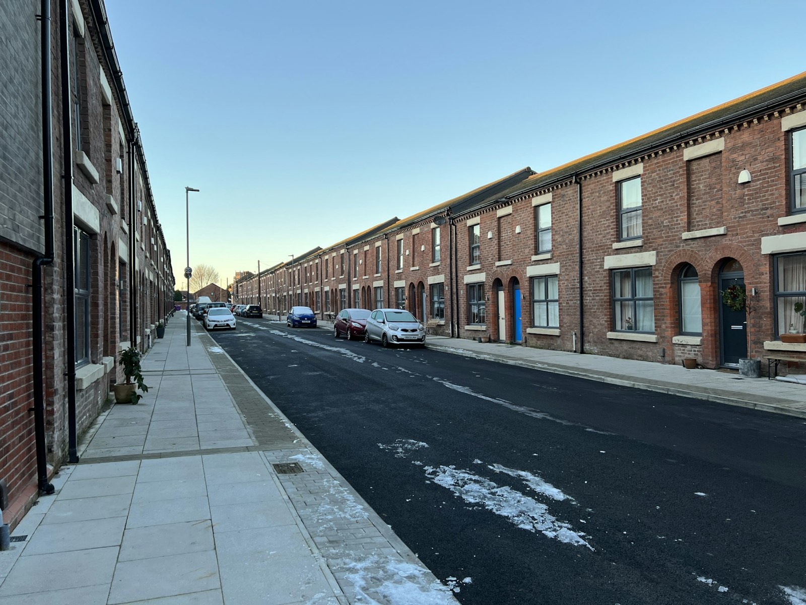 A street of Victorian brick terraced houses with cars parked along the kerb, typical solid-wall retrofit stock